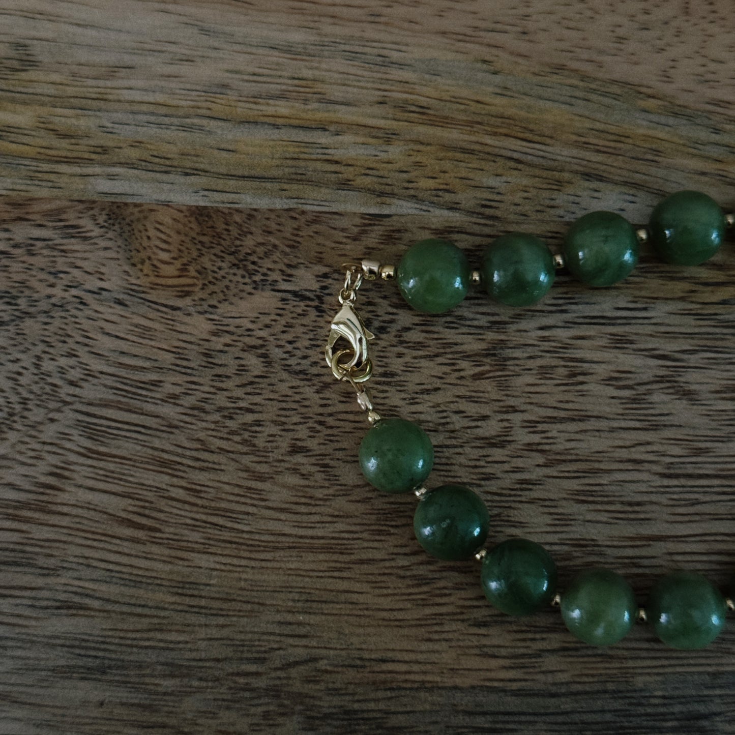Green beaded necklace with a gold clasp on a wooden surface
