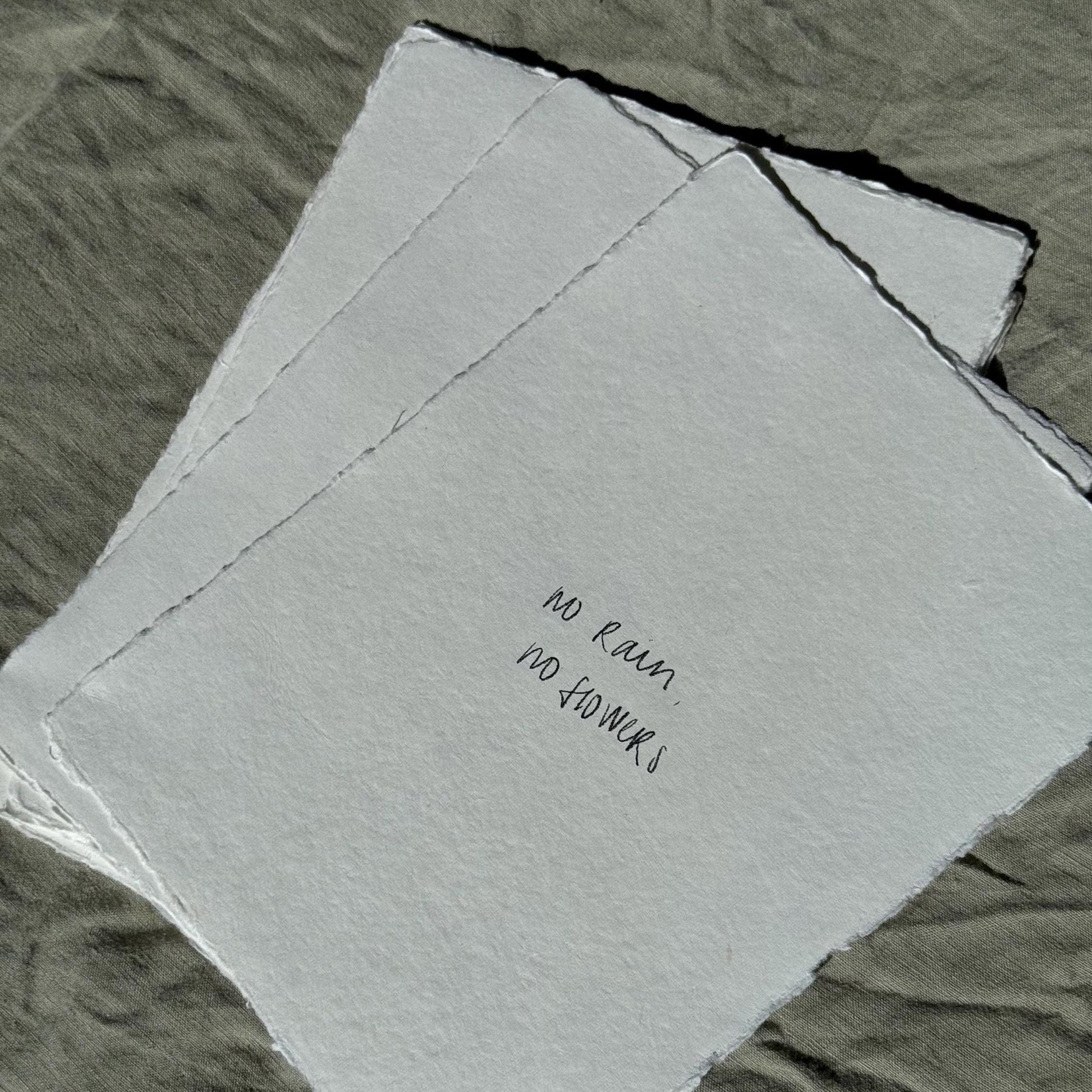 Stack of No Rain, No Flowers wall art prints on white handmade paper