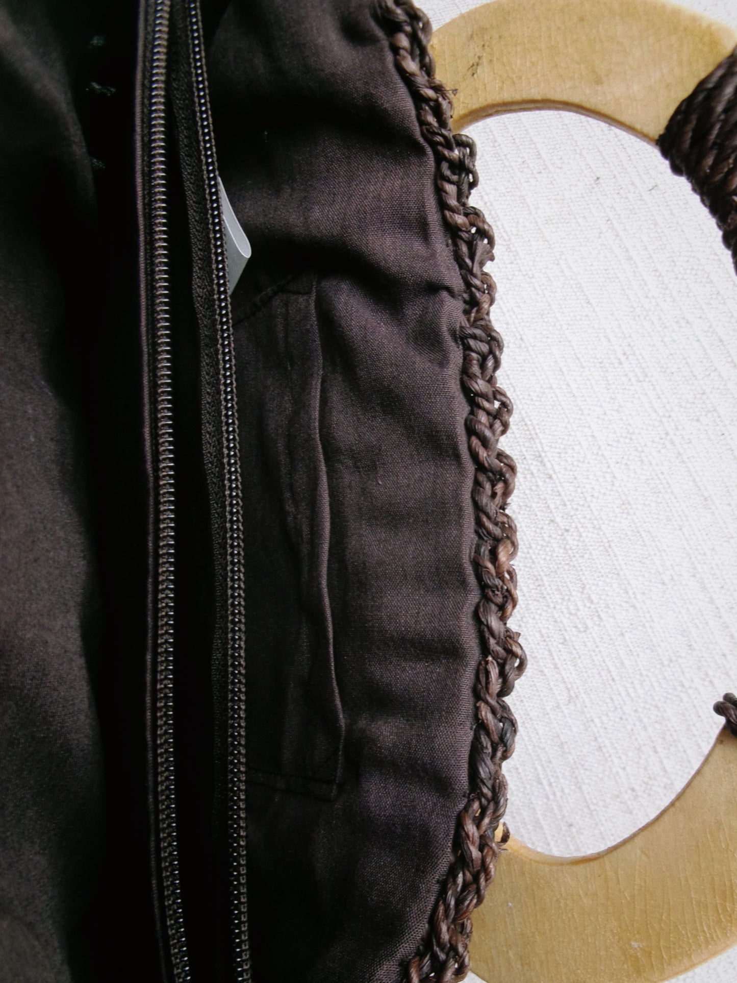 Close-up of a dark brown leather jacket with braided trim on a white background